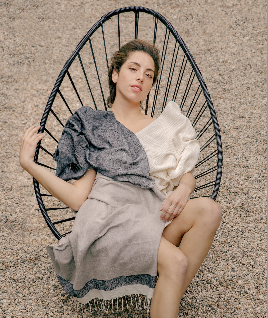 A model relaxes in a mid-century chair wrapped in our tick-repellent and mosquito-repellent Shoo for Good throw in tan and black. On one shoulder, she has our insect-repellent spruce scarf in creamy white. No need for DEET to fight ticks or mosquitoes.
