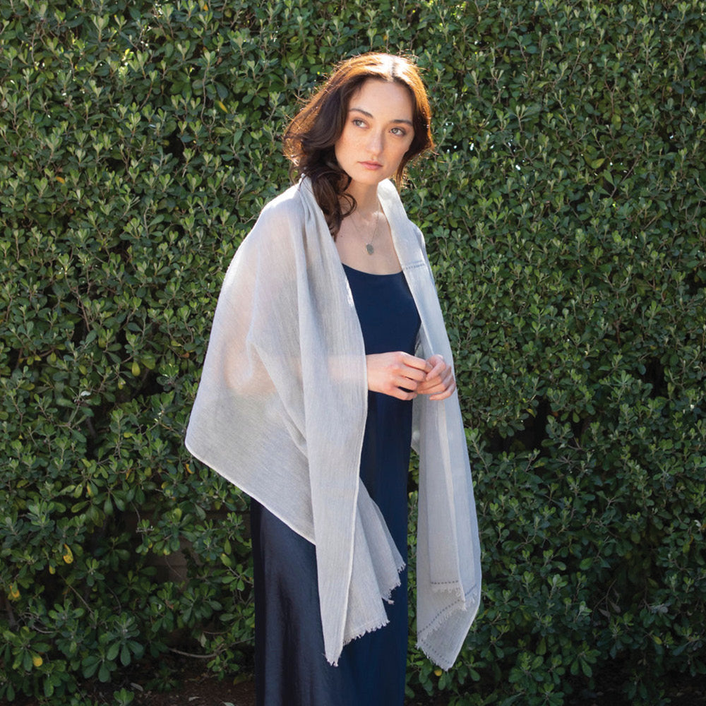 The mosquito-repellent Gardenia wrap in pale blues is ultra-lightweight, super soft, and keeps mosquitoes away. Permethrin is bound to the cotton fibers. The insect-repellency lasts for 70 washings, deterring insects for seasons. The lady wearing the wrap is relaxed in the garden, knowing bugs won't bother her. Insect Shield technology keeps bugs away.