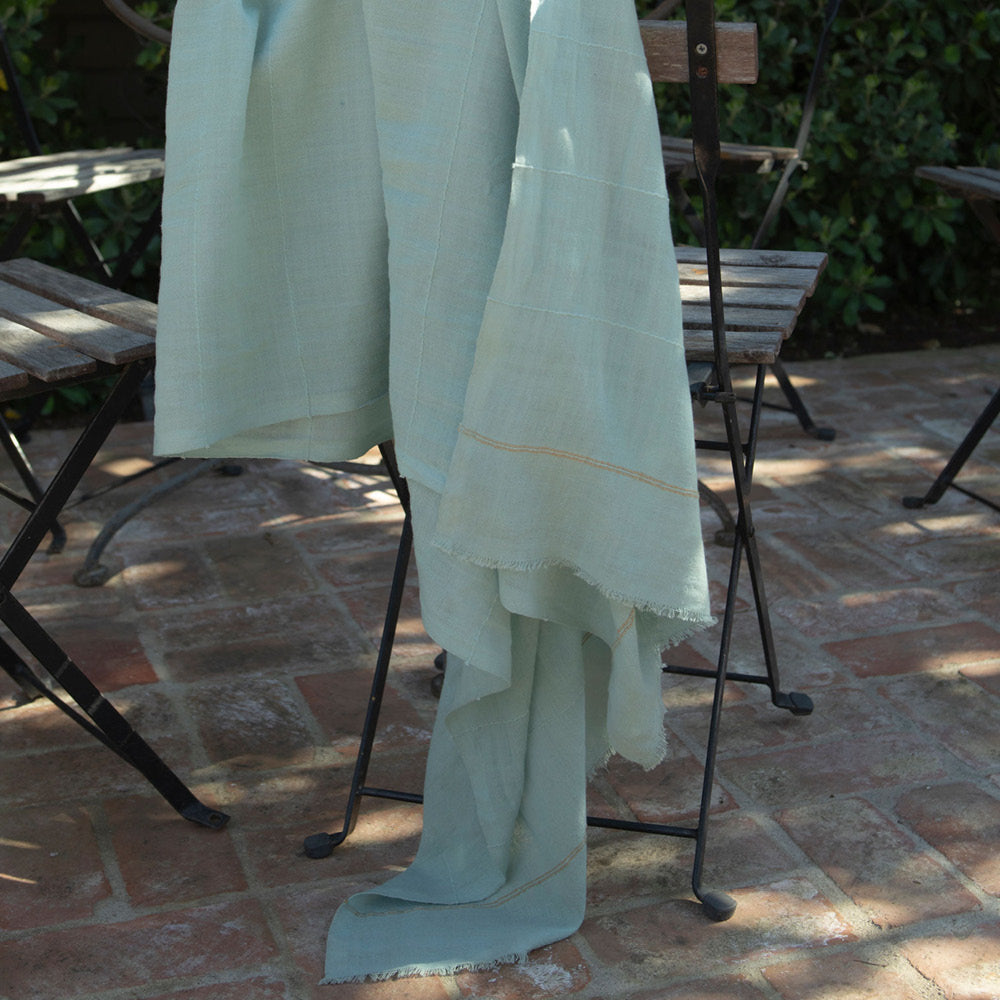 A detail photo of our mosquito-repellent Camellia shawl in sea glass green., draped over a garden chair. Insect Shield permethrin is bound to the fibers of the scarf and is effective for 70 washings. Invisible mosquito protection. An Oprah favorite.